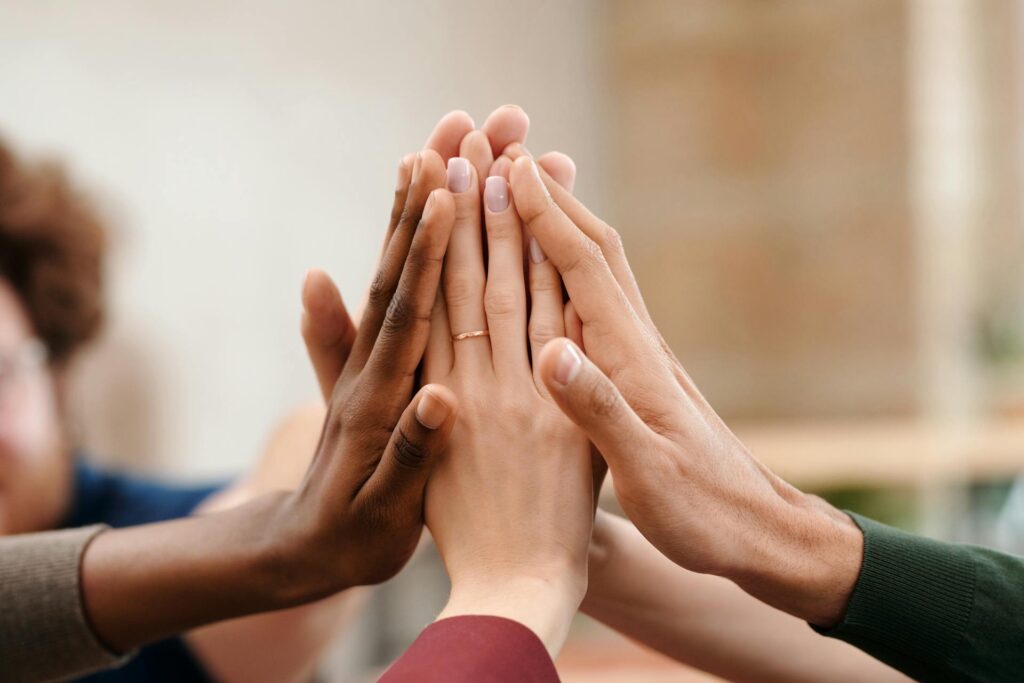 Group of diverse people joining hands together in a high-five gesture symbolizing teamwork, unity, and collaboration.