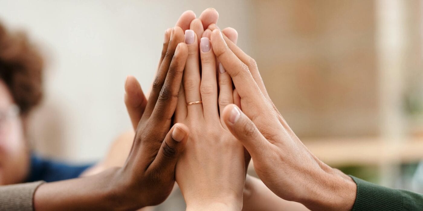 Group of diverse people joining hands together in a high-five gesture symbolizing teamwork, unity, and collaboration.